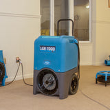 Blue Dri-Eaz LGR 7000 dehumidifier in a room with carpeted floor and white walls.