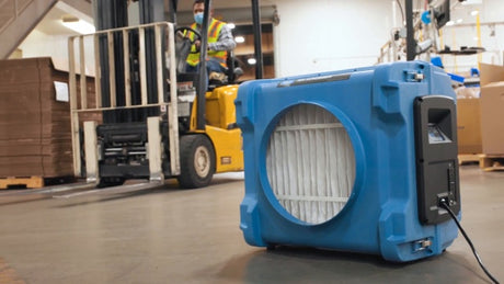 Blue industrial air filter in a warehouse setting with forklift in the background