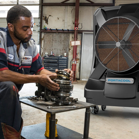 Mechanic working on a gear system in a workshop with a Portacool unit in the foreground.